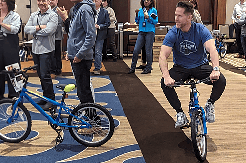 A corporate participant celebrating by riding a newly assembled bicycle through a high-energy LEVEL 12 team building workshop